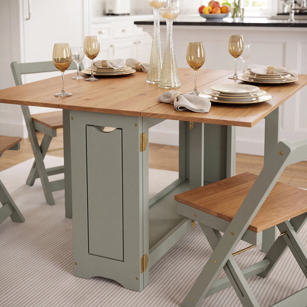 A foldable wooden dining table with sage green painted legs and matching folding chairs, styled in a bright kitchen setting with plates, wine glasses, and glassware.