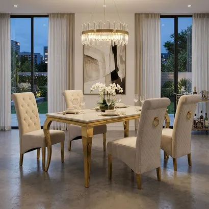 A luxury dining room set featuring a rectangular marble-top dining table with gold legs, surrounded by six tufted cream upholstered chairs with gold ring accents. The set is styled in a modern dining room with a crystal chandelier, large windows, and a concrete floor.