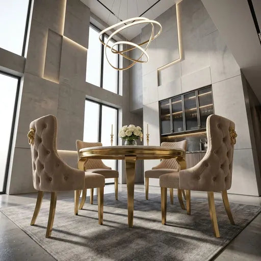 A luxury dining room set featuring a round gold table and four tufted beige velvet chairs with gold legs and decorative lion head armrests, set in a modern high-ceilinged room with geometric wall panels.