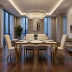 A luxury modern dining room featuring a rectangular white marble dining table with gold legs, surrounded by six tufted cream upholstered chairs. A large, multi-tiered crystal chandelier hangs from the ceiling.