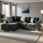 A modern L-shaped sectional sofa in dark gray and charcoal tones, styled with multiple throw pillows in a contemporary living room setting with a large light gray rug and wall art.