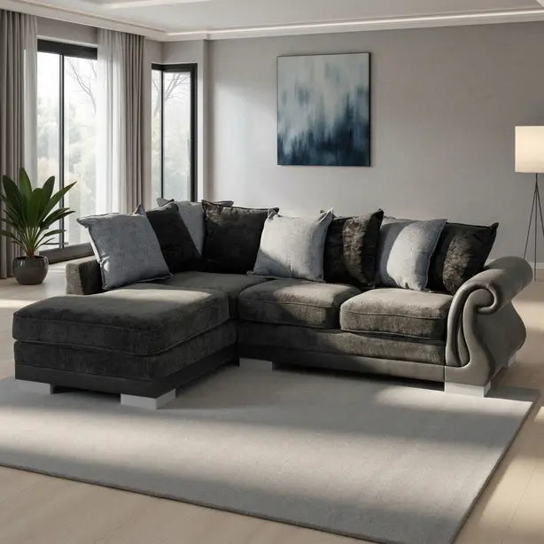 A modern L-shaped sectional sofa in dark gray and charcoal tones, styled with multiple throw pillows in a contemporary living room setting with a large light gray rug and wall art.
