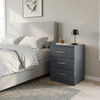A modern three-drawer nightstand in dark gray with silver handles, positioned next to a light gray 
