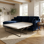 A navy blue sectional sofa with a chaise lounge and an off-white mattress on a metal frame, shown in a bright, modern living room setting.