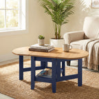 A round coffee table with a light natural wood top and navy blue legs, styled in a bright living room with a plant, armchair, and woven rug.