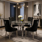 A round dining table with a dark marble-patterned top and chrome legs, surrounded by four black upholstered dining chairs with silver ring pulls, set in a modern dining room with a chandelier, rug, and wall art.