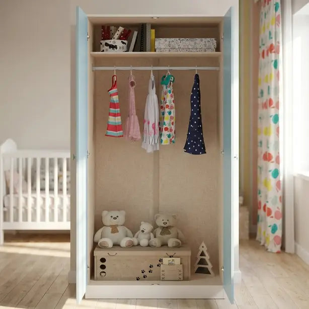 A tall children's wardrobe with light blue doors and a beige interior, shown open in a nursery. The wardrobe contains several colorful dresses hanging on hangers, a storage box with stuffed teddy bears, and a small wooden toy on the bottom shelf.