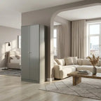 A tall, minimalist two-door cabinet in a matte gray finish stands in a modern living room setting next to a beige sectional sofa and wooden coffee table.