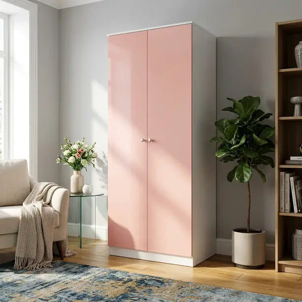 A tall two-door wardrobe in a glossy light pink finish with silver knobs, set in a modern living room next to a sofa, side table, potted plant, and wooden bookshelf.
