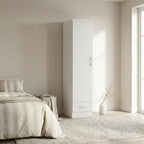 A tall white single-door wardrobe with a silver handle and a bottom drawer, shown in a bright, modern bedroom next to a bed and rug.