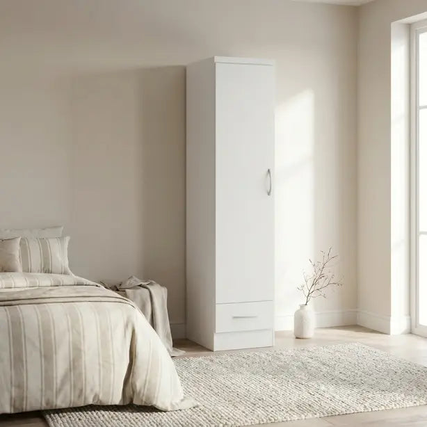 A tall white single-door wardrobe with a silver handle and a bottom drawer, shown in a bright, modern bedroom next to a bed and rug.