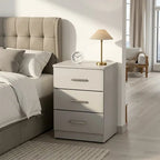 A three-drawer nightstand in a light gray finish with silver handles, styled next to a bed in a modern bedroom. A small table lamp and a round clock sit on top of the nightstand.