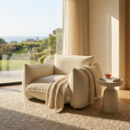 Beige armchair with a blanket in a sunlit room with large windows.