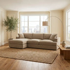 Beige sectional sofa in a living room with large windows and a plant.