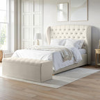 Beige upholstered bed in a bright bedroom with large windows.