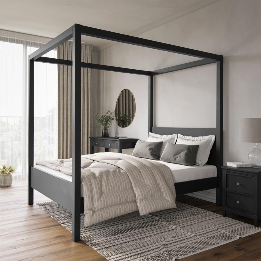 Black canopy bed in a bedroom with wooden flooring and a mirror on the wall.