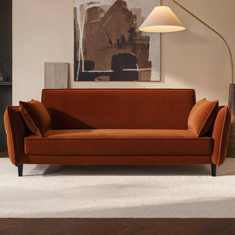 Burnt orange sofa in a room with abstract art and a lamp.