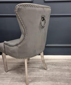 Gray upholstered chair with nailhead trim and a ring handle against a dark blue wall.