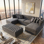 Gray sectional sofa with tufted ottoman in a room with large windows and cityscape view.