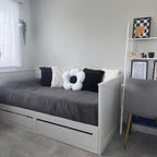 Gray daybed with decorative pillows in a room with a white wall and a shelf.
