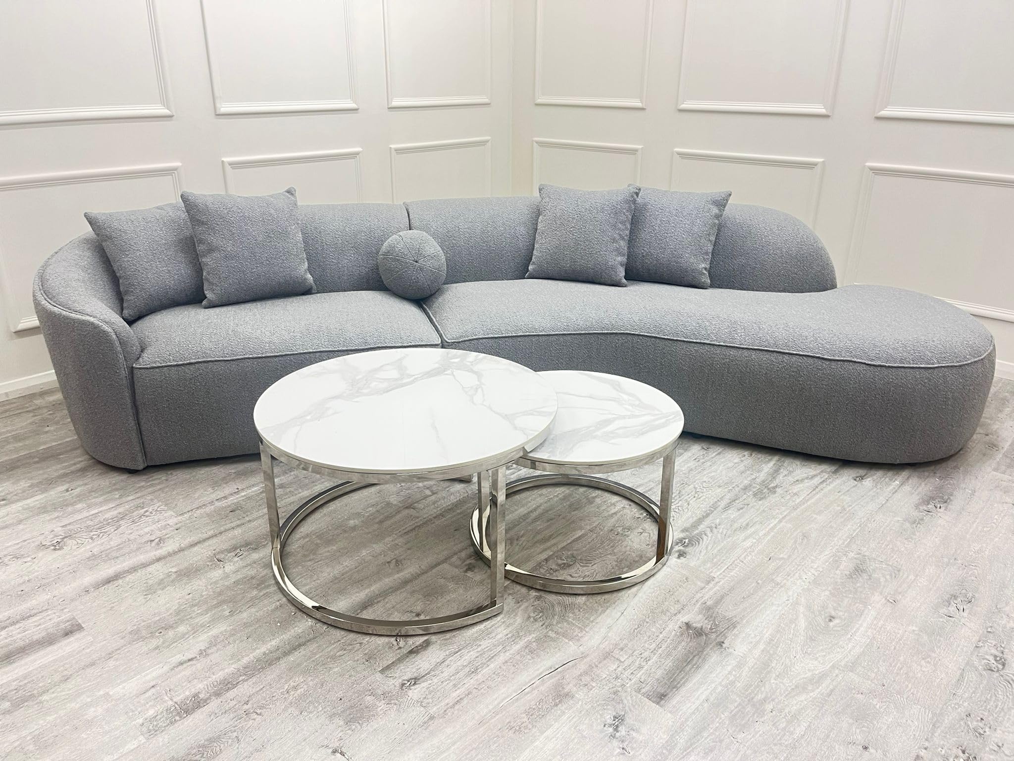 Gray sectional sofa with two round coffee tables on a light wood floor.