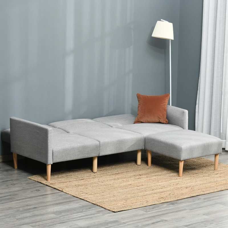 Gray sectional sofabed with a brown pillow on a wooden floor in a room with gray walls and a lamp.