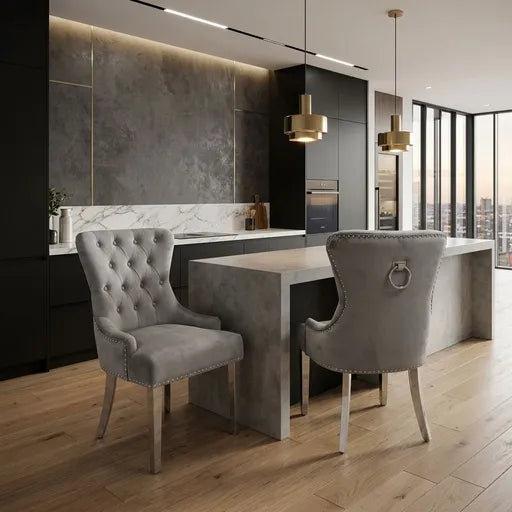 A modern kitchen and dining area featuring two tufted gray velvet dining chairs with silver nailhead trim and light wood legs