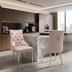 Two elegant blush pink upholstered dining chairs with silver metal legs, displayed in a modern kitchen setting with a marble island and dark wood cabinetry.