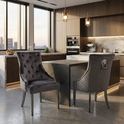 Two modern gray upholstered dining chairs in a stylish kitchen setting. One chair is tufted velvet, and the other is quilted with a lion head ring pull, set around a dark metal dining table.