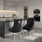 Two modern tufted dining chairs with black quilted upholstery, silver lion head ring pulls, and silver legs, positioned at a kitchen island in a contemporary kitchen setting.