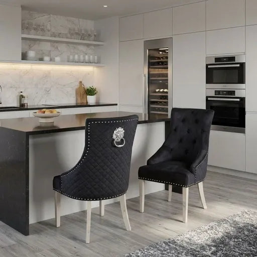 Two modern tufted dining chairs with black quilted upholstery, silver lion head ring pulls, and white legs