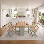 A dining set consisting of a rectangular light wood table and four matching folding chairs in a sage green finish, set on a white textured area rug in a bright, modern kitchen.
