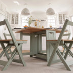 A light sage green folding dining table with a natural wood top, accompanied by matching folding chairs in a bright, modern kitchen setting.