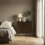 Modern bedroom with a bed, nightstand, lamp, and plant against a neutral wall.