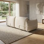 Modern beige sofa in a living room with large windows and neutral decor.