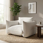 Modern white armchair in a living room with a plant and framed picture on the wall.