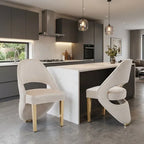 Two modern curved dining chairs with textured cream upholstery and gold legs, positioned at a white marble kitchen island in a contemporary kitchen setting.