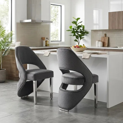 Two modern gray upholstered dining chairs with sculptural curved backs and silver metal legs, placed at a white kitchen island in a bright contemporary kitchen.