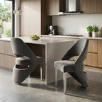 Two modern gray upholstered dining chairs with sculptural curved backs and slim metallic legs, placed at a kitchen island in a contemporary kitchen setting.