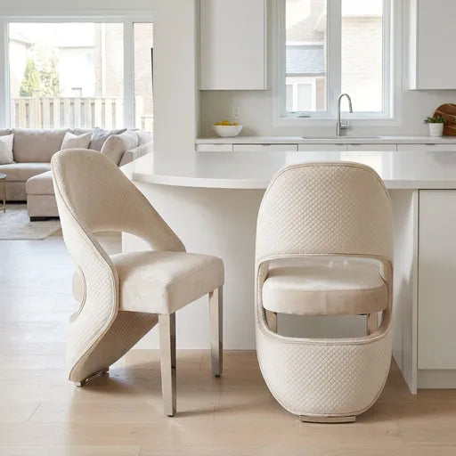 Two modern upholstered dining chairs in a warm cream fabric with a quilted texture, shown in a bright, contemporary kitchen setting.