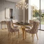 A luxury dining set featuring a rectangular black glass-top table with a gold frame and four tufted blush pink velvet chairs with gold lion head accents on the backrests, set in a modern dining room with wood floors and a concrete wall.