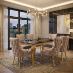 An elegant dining room set featuring a rectangular black marble-top dining table with a gold frame, surrounded by six tufted blush pink velvet chairs with gold legs, set on a patterned oriental rug.