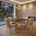 A luxury dining room set featuring a rectangular black marble-top table with gold legs, surrounded by six tufted cream velvet chairs with gold accents, set in a modern high-end interior with a marble wall and fireplace.