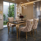 A luxury dining room set featuring a rectangular table with a black glass top and gold legs, surrounded by four tufted blush pink velvet chairs with gold lion head accents, set in a modern interior with a slatted wood accent wall.