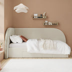 Beige bed in a room with a beige wall and white rug.