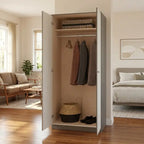  organizer stands open in a staged bedroom/living space. The cabinet has a light gray exterior and beige interior, with a hanging rod holding three garments, a folded stack on top, and a woven basket and shoes on the bottom shelf.