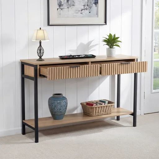 A modern console table with a light oak wood finish, black metal legs, and fluted drawer fronts. 