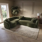 A curved olive green velvet sectional sofa with matching throw pillows, styled in a modern living room setting on a textured beige rug.