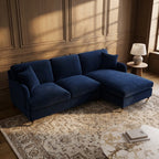 A dark blue velvet sectional sofa with a chaise lounge, styled in a warm, wood-paneled room on a patterned rug with a side table and lamp.