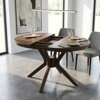 A dark brown wooden extendable dining table with a unique star-shaped pedestal base, shown in a modern dining room setting with two gray upholstered chairs and place settings on the tabletop.